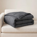 Couverture lestée gris anthracite pliée sur un canapé blanc cassé, matelassage en carrés