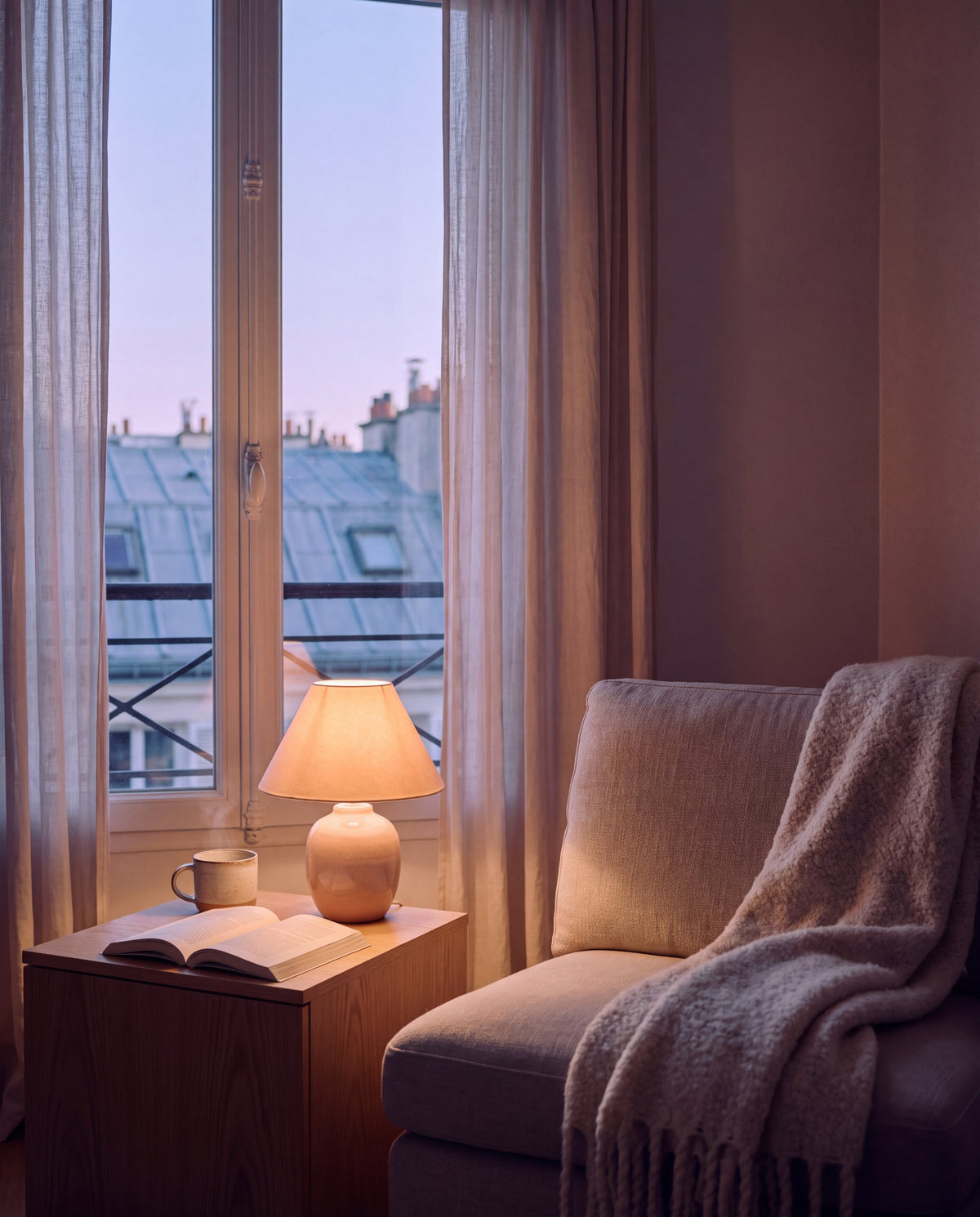 Salon parisien à l’heure bleue, lampe allumée et plaid en laine sur un fauteuil en lin